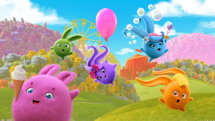 Round, fluffy characters in different colours jumping across a green field with a blue sky in the background.